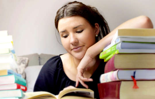 a young woman peacefully reading a book with her arm resting a whole stack of books